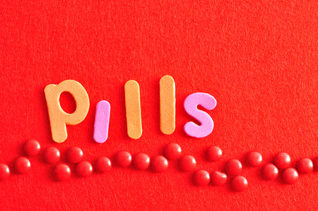 A row of red pills on a red background with the word pillsの写真素材