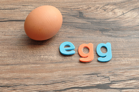 A single chicken egg with the word egg displayed on a wooden tableの写真素材