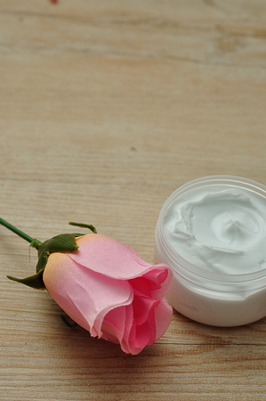 A pink artificial rose with a jar of white body lotionの写真素材