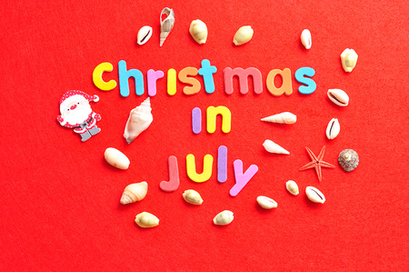 Christmas in July on a red background with a collection of shells and a Santa Clause figureの写真素材