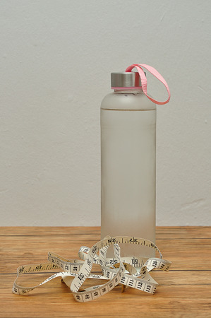 A glass bottle filled with ice cold water and a measuring tapeの写真素材