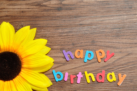 Happy birthday in colorful letters displayed with an artificial sunflowerの写真素材