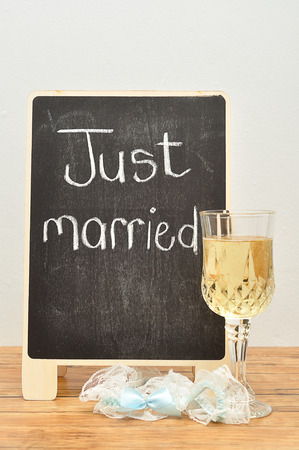 A blackboard with just married on it displayed with a glass of champagne and a garterの写真素材
