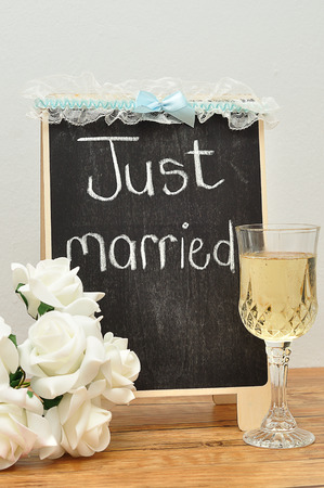 A blackboard with just married on it displayed with a glass of champagne, a bunch of roses and a garterの写真素材