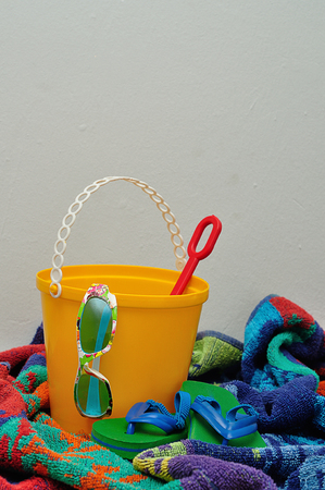 A plastic bucket displayed with a towel. spade, shoes and sunglassesの写真素材