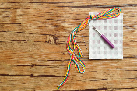 String of colorful embroidery thread displayed with a piece of embroidery fabric, a needle and a pickerの写真素材