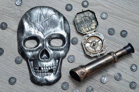 A skull mask, compass and an eyeglass with toy pirate coinsの写真素材