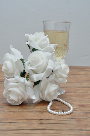 A glass of champagne, white roses and a string of pearlsの写真素材