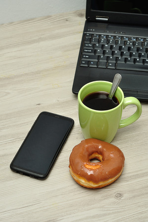 A cellphone, laptop, doughnut and cup of coffeeの写真素材
