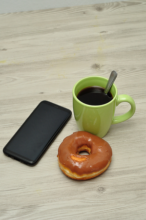 A cellphone, doughnut and cup of coffeeの写真素材