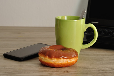 A cellphone, laptop, doughnut and cup of coffeeの写真素材