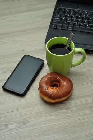 A cellphone, laptop, doughnut and cup of coffeeの写真素材