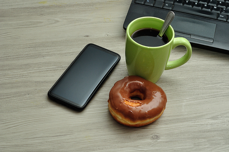 A cellphone, laptop, doughnut and cup of coffeeの写真素材