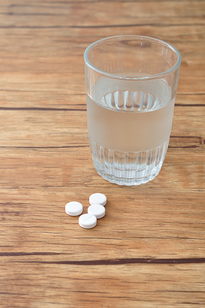 White pills displayed with a glass of waterの写真素材
