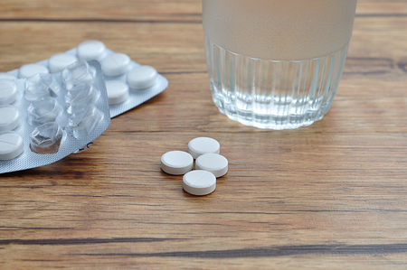 White pills displayed with a glass of water and two blister packsの写真素材