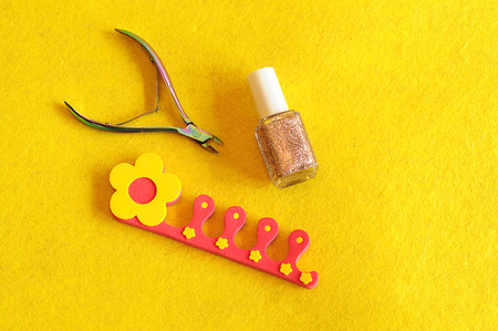 Nail clipper, polish and toe separator on a yellow backgroundの写真素材