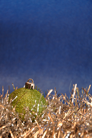 A single green Christmas bauble with silver tinsel against a blue backgroundの写真素材