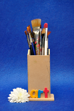 A collection of different size paint brushes in a wooden container with a white aster and the word artの写真素材