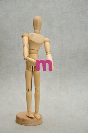 A wooden mannequin holding a letter mの写真素材