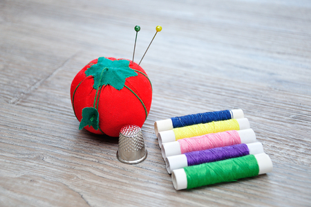 Rolls of thread with an out of focus pin cushion shaped as a red tomato and a thimbleの写真素材