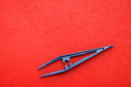 A blue plastic tweezers isolated on a red backgroundの写真素材