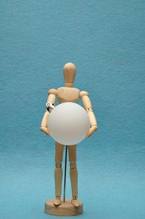 A wooden art mannequin holding a white Christmas baubleの写真素材