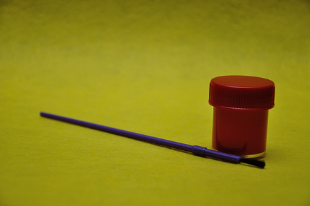 A pot of red paint with a purple paintbrush on a yellow backgroundの写真素材