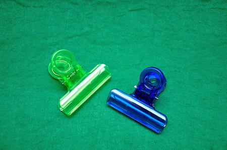 Two colorful plastic bulldog clips on a green backgroundの写真素材