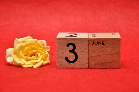3 June on wooden blocks with a yellow rose on a red backgroundの写真素材