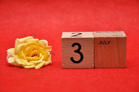 3 July on wooden blocks with a yellow rose on a red backgroundの写真素材