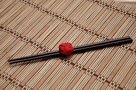 A pair of red chopsticks tied together on a bamboo place matの写真素材