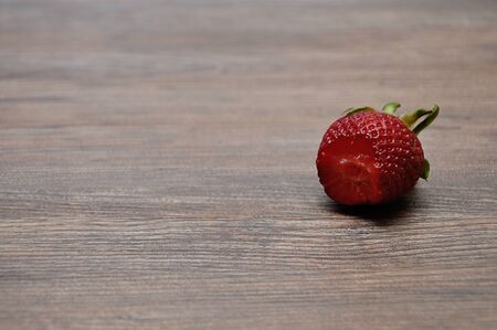 A strawberry with a bite out on a wooden backgroundの写真素材