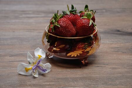A bowl of strawberries displayed with an African Iris on a wooden backgroundの写真素材