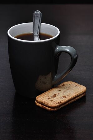 A mug of black coffee with a stack of biscuitsの写真素材