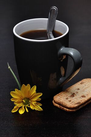 A mug of black coffee with a stack of biscuits and a yellow flowerの写真素材