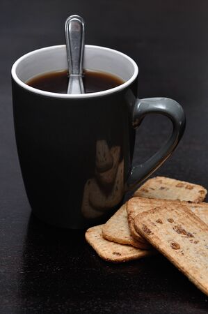 A mug of black coffee with a stack of biscuitsの写真素材