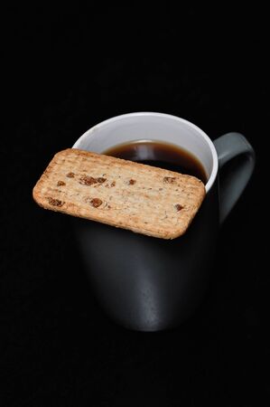 A mug of black coffee with a biscuit on topの写真素材