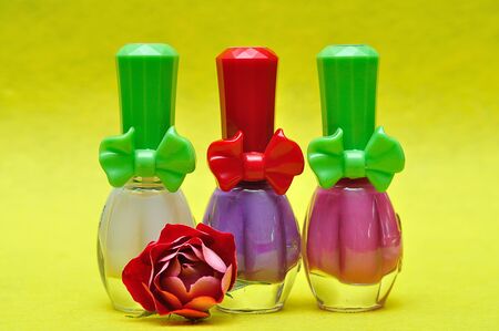 A row of different color nail polish on a yellow background with a red roseの写真素材