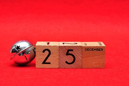 25 December on wooden blocks with a silver bell on a red background