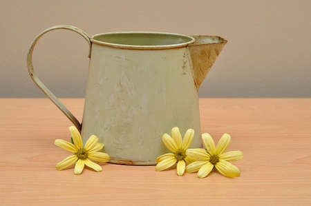 A rusty old mug on a table with yellow daisiesの写真素材