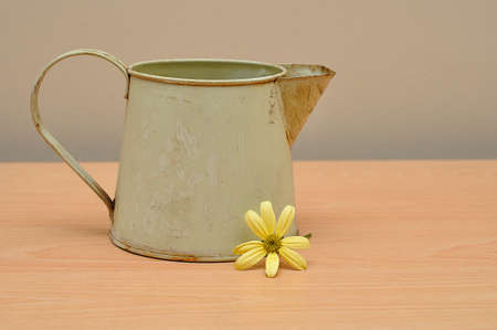 A rusty old mug on a table with a yellow daisyの写真素材