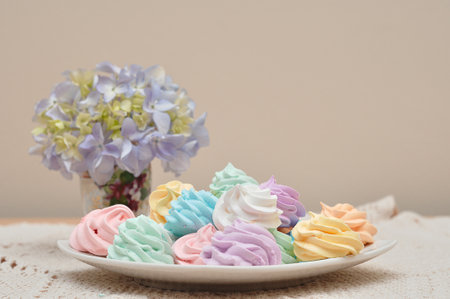 A plate of meringues with an out of focus display of hydrangeasの写真素材