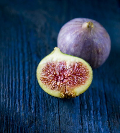 Whole figs and one fig sliced  on top of wooden table. Focus is on the sliced figの写真素材