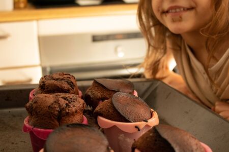 Little daughter with a chocolate stained face and smiling next to the dessert she has made with her...