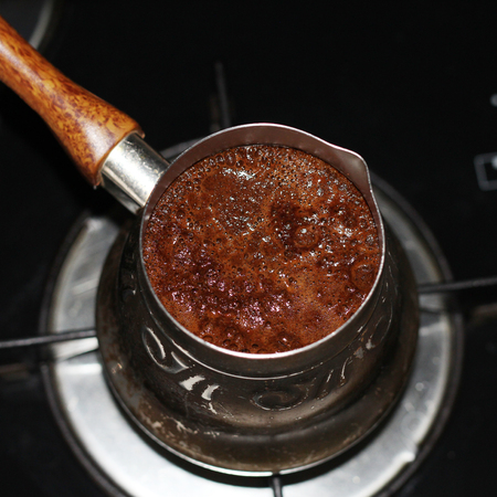Coffee is prepared in the turka, coffee pot, coffee maker, at home. It boils, foam appears. Turka for coffee is on the stove.の写真素材