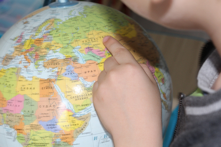 The child is studying geography. Finger pointing to the globe. Children's hand on the background of the card.の写真素材