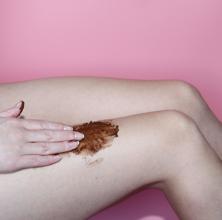 A female hand applies a scrub of ground coffee to her feet. A scrub of coffee grounds is applied on the feet. Peeling. Skin care.の写真素材
