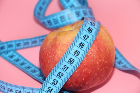 Blue tape for measuring the body around an apple. Apple on a pink background. The concept of losing...