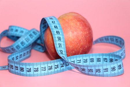 Blue tape for measuring the body around an apple. Apple on a pink background. The concept of losing...