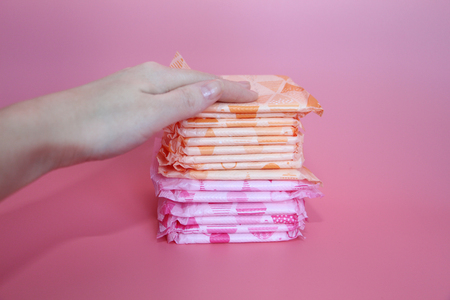 A beautiful female hand rests on several sanitary pads. Pink background. Many feminine hygiene pads.の写真素材